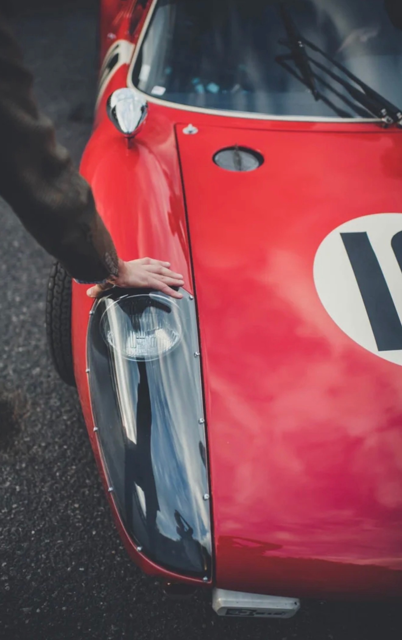 A hand resting on a vintage race car's fender